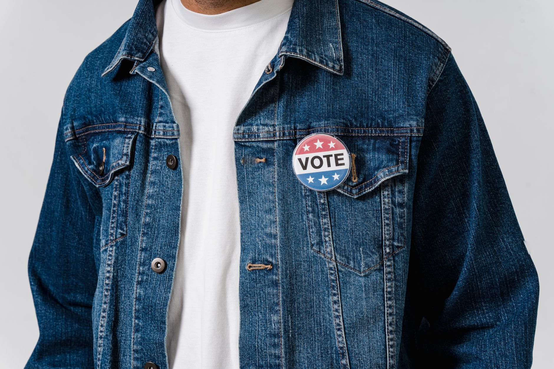 Close-up of a denim jacket with a patriotic vote badge promoting political engagement.