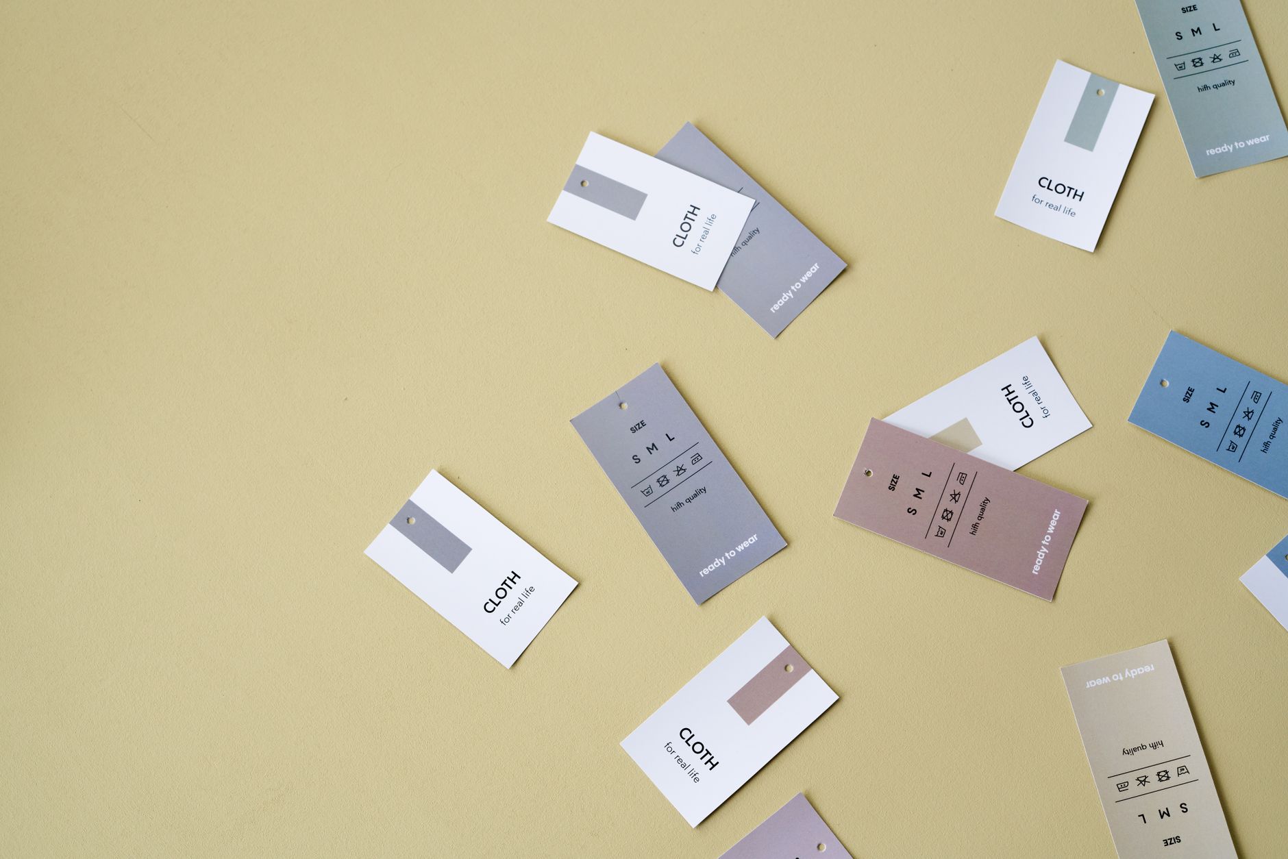 Floating clothing tags in various colors against a yellow backdrop with ample copy space.