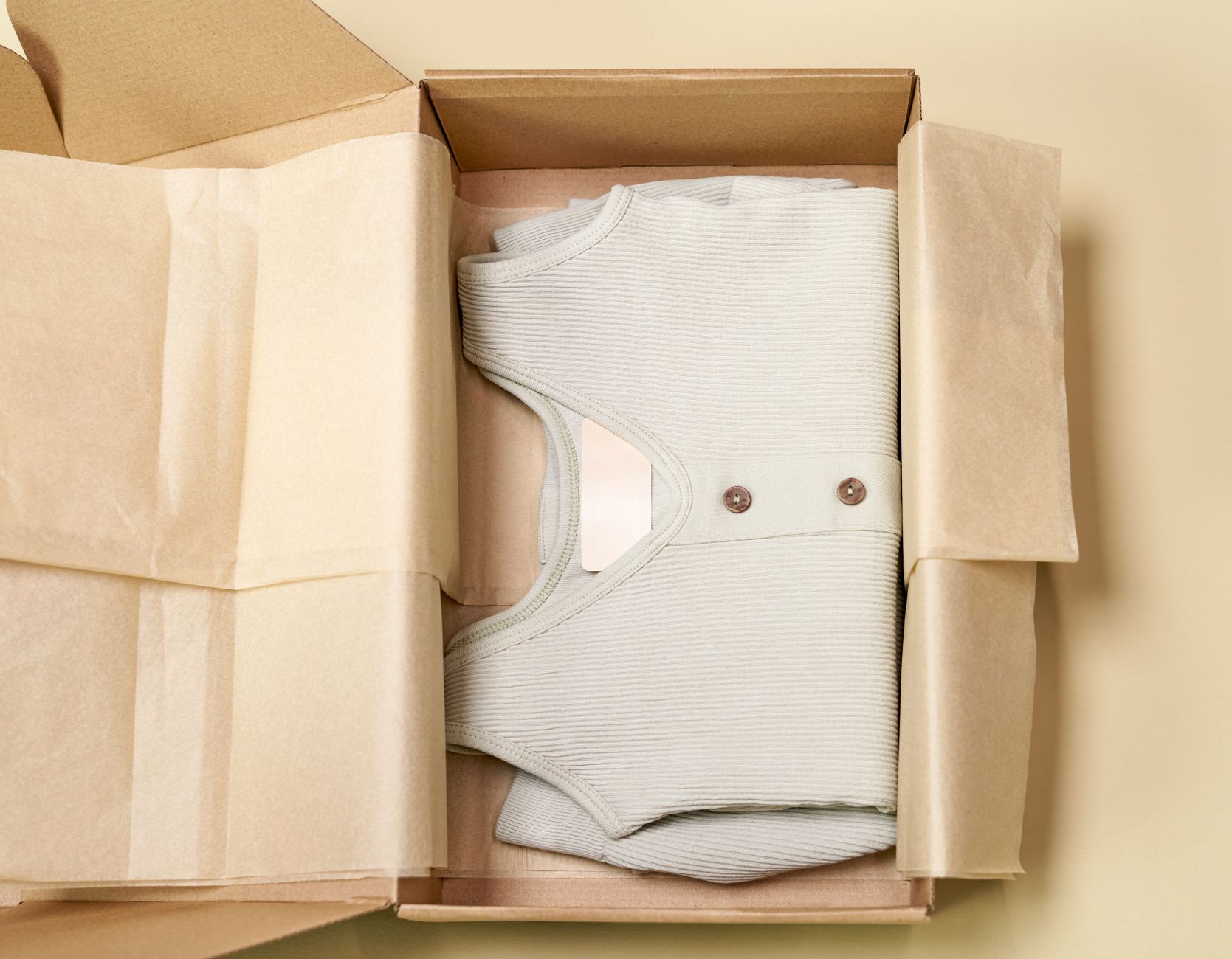 Minimalist packaging showcases a ribbed beige garment neatly folded inside a cardboard box.