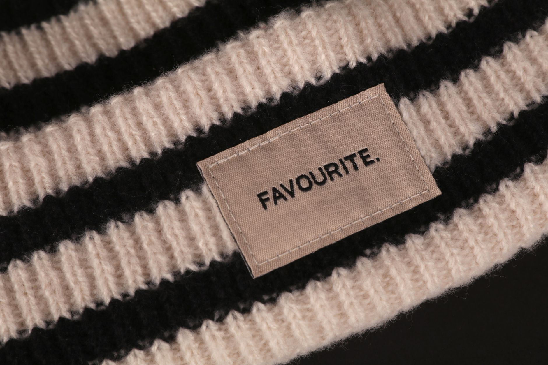 Detailed view of striped wool fabric with an embroidered 'FAVOURITE' label, minimal style.