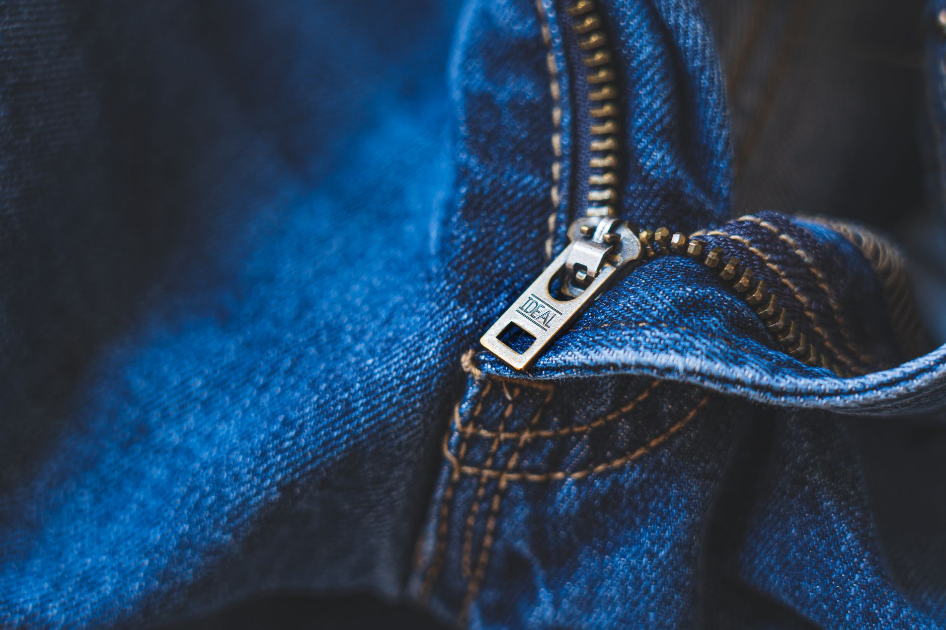 Close-up of blue denim fabric featuring a metal zipper with detailed stitching.