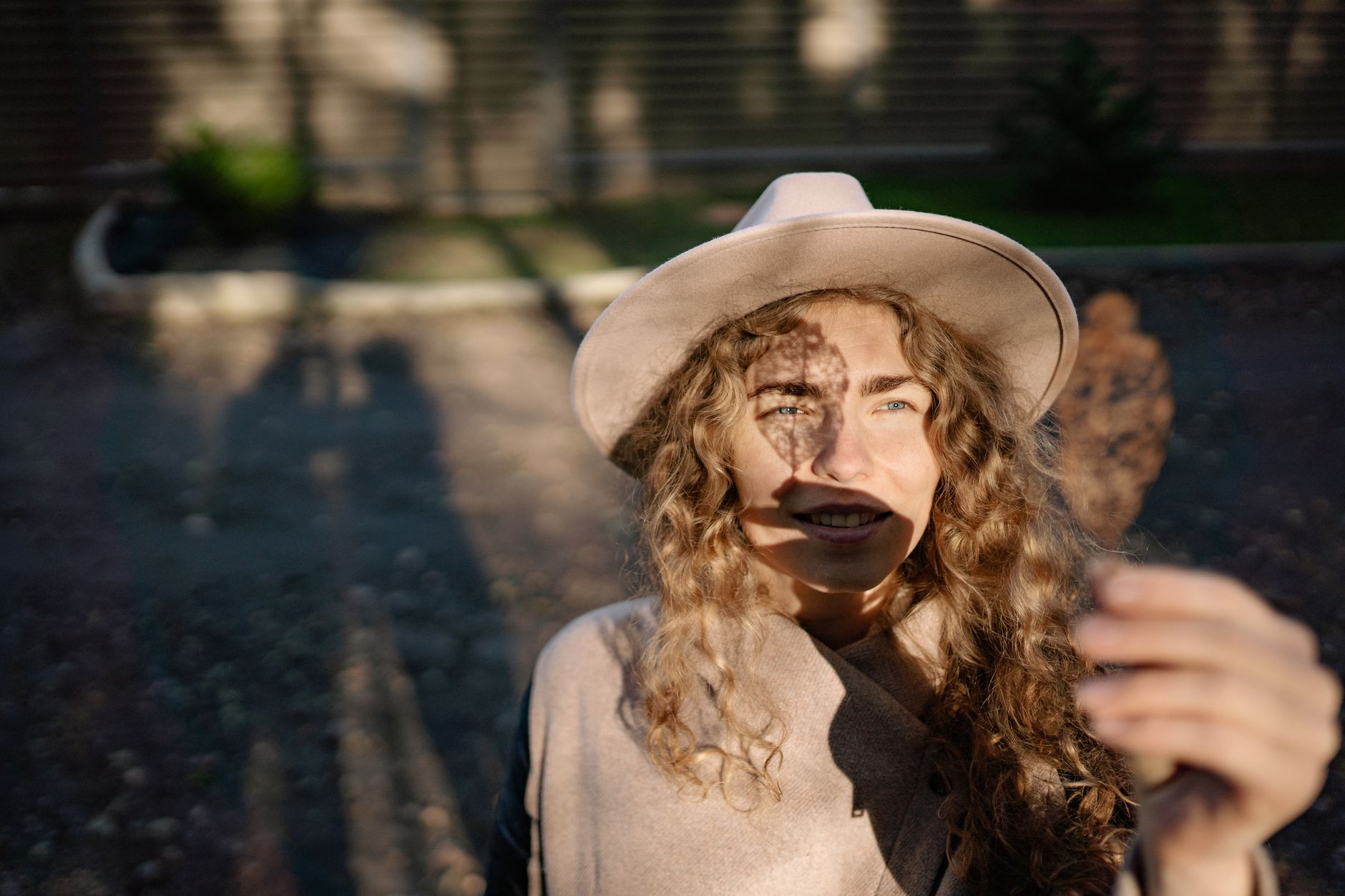 A woman in a wide brim hat enjoys the autumn sunlight, holding a leaf and casting a shadow.