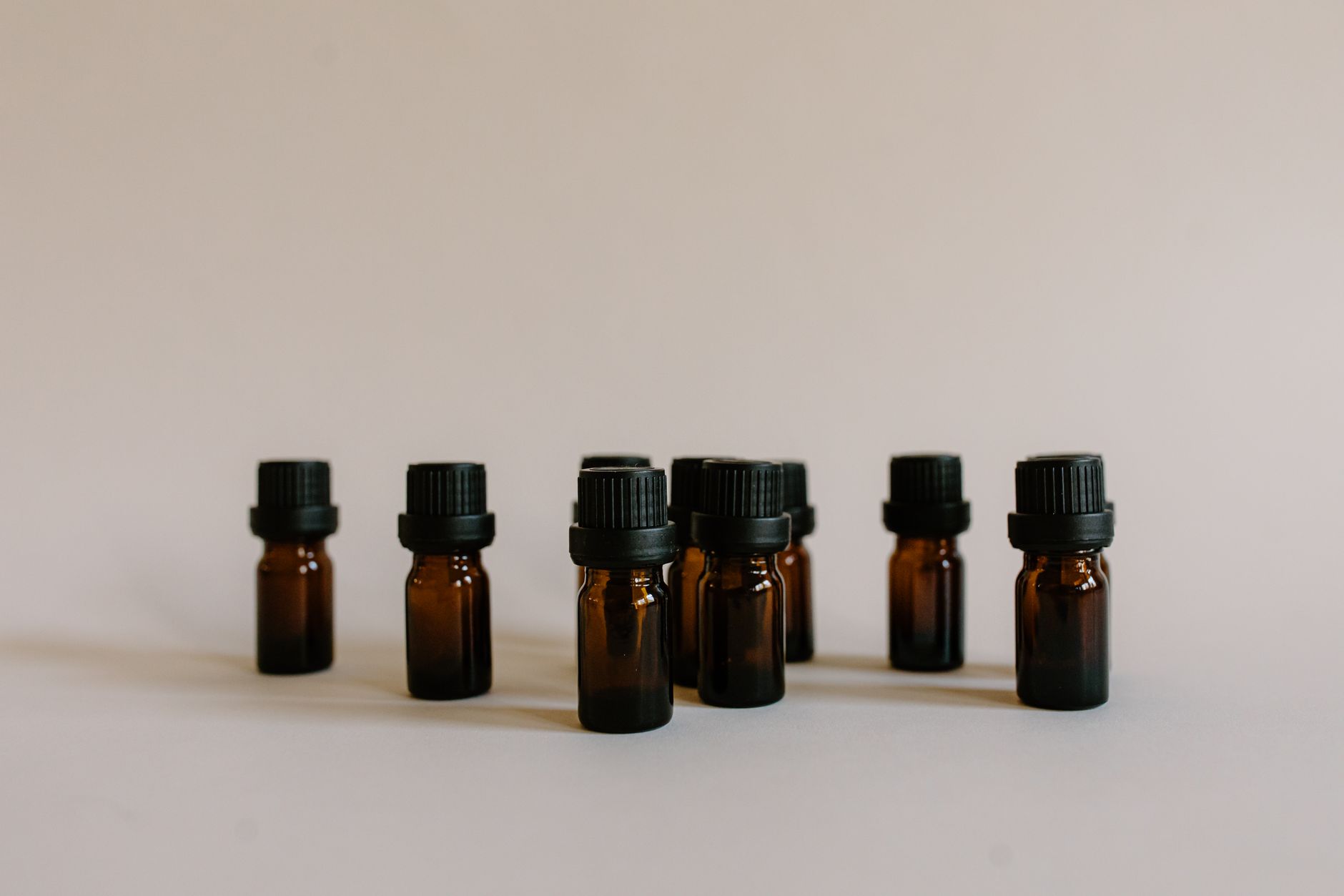 A minimalist still life featuring multiple amber essential oil bottles with black caps on a neutral background.