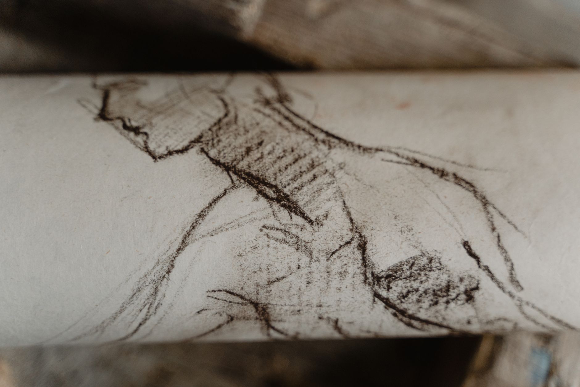 Gros plan d’un rouleau de papier clair portant un croquis rapide aux traits sombres et hachurés, avec d’autres rouleaux flous derrière.