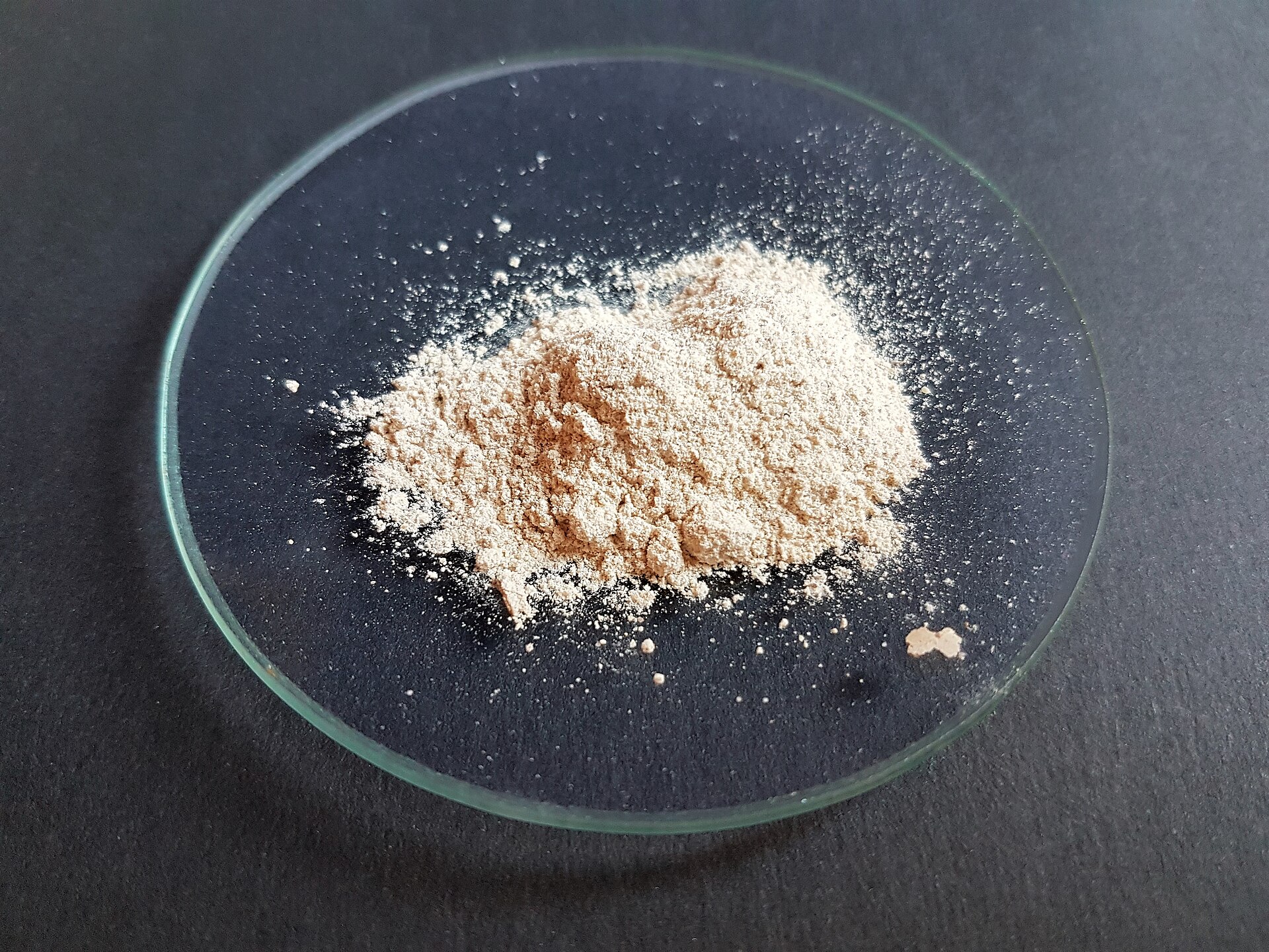 Ingrédient cosmétique en poudre beige, un son d'amande mêlé de sable fin, étalé dans une coupelle de verre